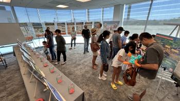 A display in an indoor space with posters on easels and photographs set up on tables, where a crowd of people is looking at the various displays.