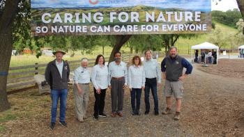 Seven Open Space Authority directors standing in a line and smiling at the camera, under a large banner that says "Caring for Nature, So Nature Can Care for Everyone"