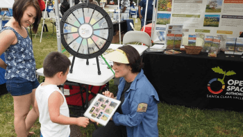 One adult and one child engage with an Open Space Authority representative at a community outreach booth