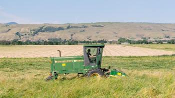 A person on a tractor driving through a hay field with golden hills in the background