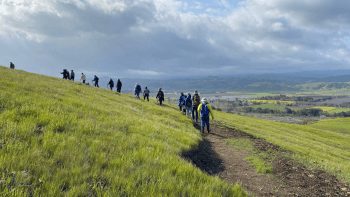 Group of hikers rounding a green hill (Photo by Livia Lu)