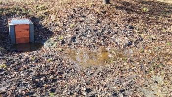 A weir sits in the ground next to a small pool of water