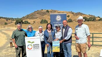 A group of seven adults stand in behind a white podium with the Open Space Authority logo, in front of a partially covered banner that says 'U.S. Representative Jimmy Panetta."