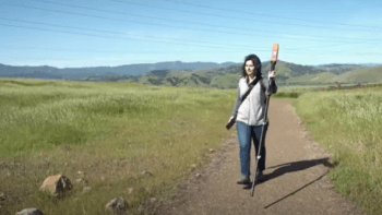 Woman walking with mapping tool on trail with green hills and blue sky