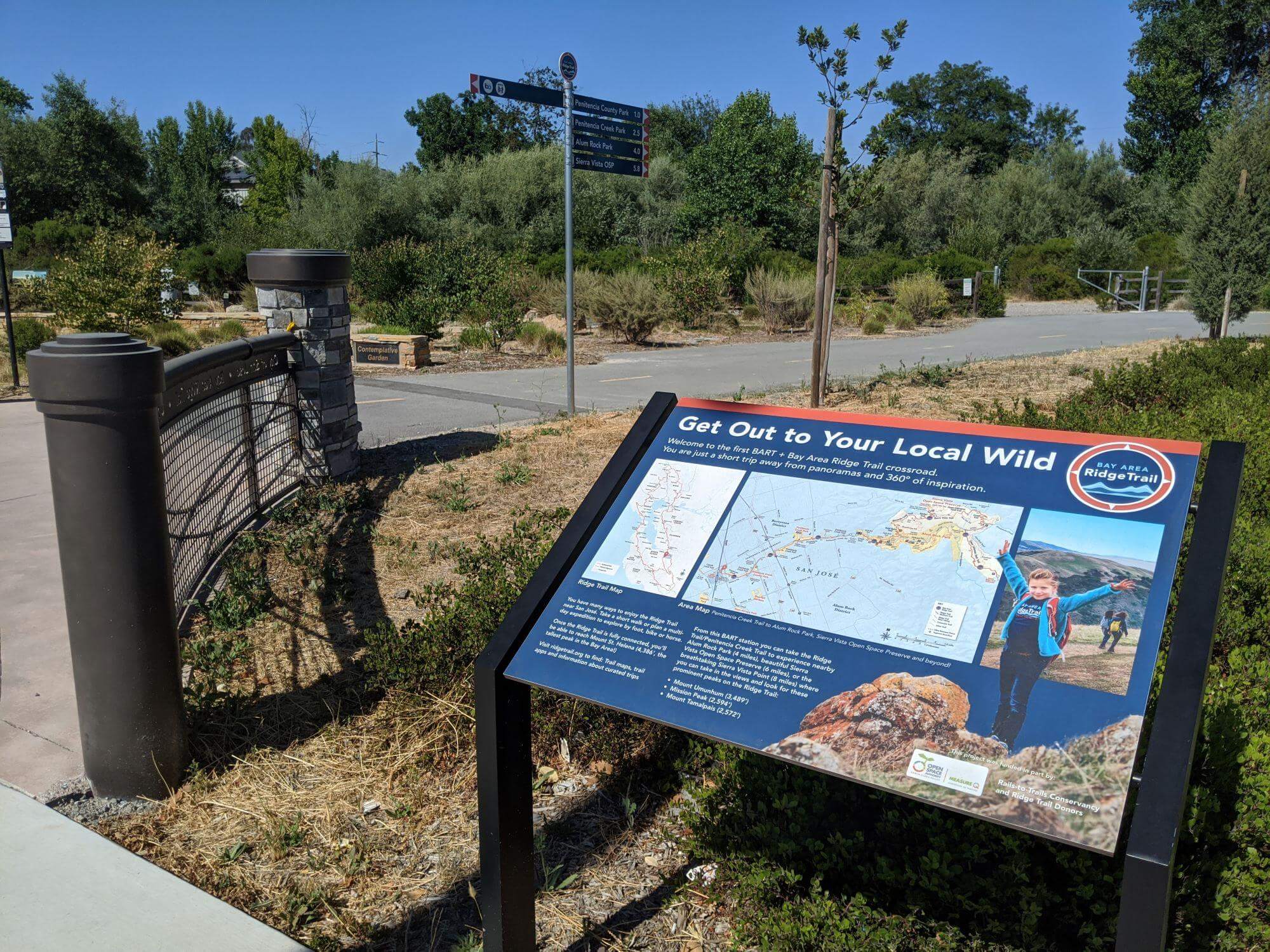 A large educational panel with the title "Get out to your local wild" above a map of the Bay Area, next to a paved trail and wayfinding signage