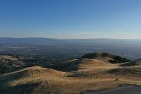 An aerial view of Sierra Vista's rolling gold hillsides with trails winding across them. Beyond the hills is an expansive view of Santa Clara Valley below, under a clear blue sky.